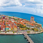 Curaçau é uma ilha localizada no sul do Caribe, próximo à costa da Venezuela. É um destino popular de turismo, conhecido por suas praias de areia branca, águas cristalinas, cultura diversa e arquitetura colorida. A capital de Curaçao, Willemstad, é famosa por sua arquitetura holandesa colonial, que lhe rendeu a designação de Patrimônio Mundial da UNESCO. A cidade também abriga muitas lojas, restaurantes e bares que oferecem uma mistura única de culinária local e internacional. As praias de Curaçao são outro grande atrativo turístico, com águas claras e calmas ideais para a prática de snorkeling e mergulho. Curaçao é conhecida por sua atmosfera descontraída e amigável, o que a torna um destino popular para casais, famílias e viajantes solo. Com suas praias deslumbrantes, rica cultura e arquitetura vibrante, Curaçao é um destino turístico ideal para quem procura um paraíso tropical com uma pitada de história e cultura.